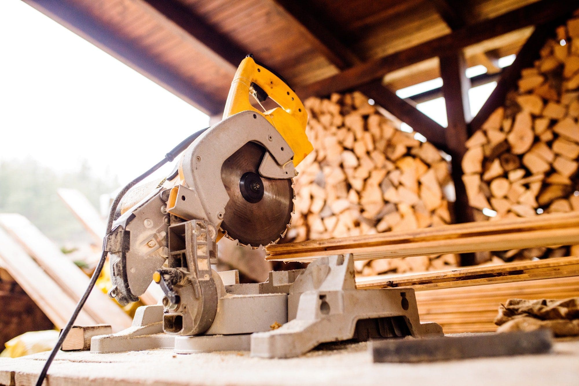 Circular saw laid on table, stack of wood behind it